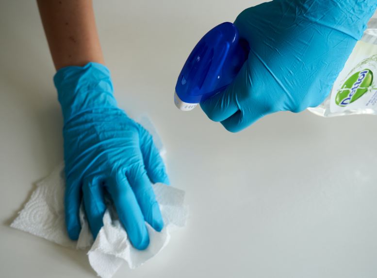 A person wearing blue gloves, sanitizing a white surfaces
