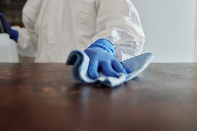A person cleaning a table in protective gear.