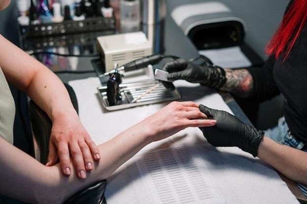 A person wearing black disposbale gloves filling the nails of a woman