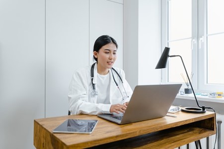 a doctor sitting at her desk and looking at her laptop in a clean and safe workplace